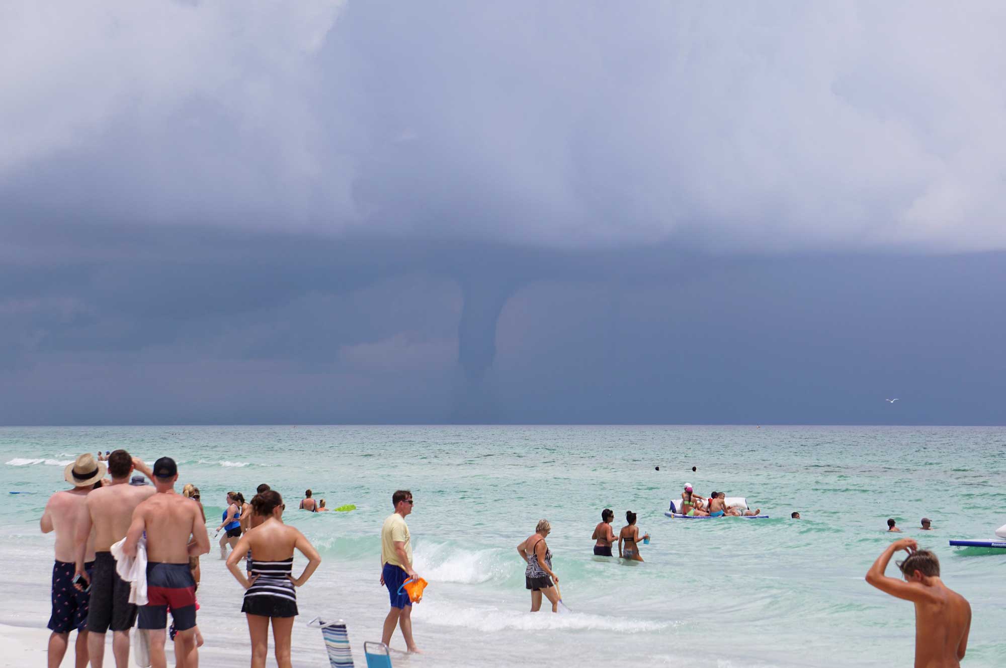 Photograph of people at a beach in Florida watching a waterspout over the ocean.