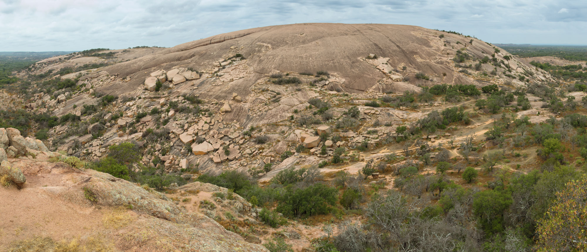Photo of Enchanted Rock, a Precambrian granitic dome in Texas. The rock is dome-shaped and tan in color. It shows signs of weathering.