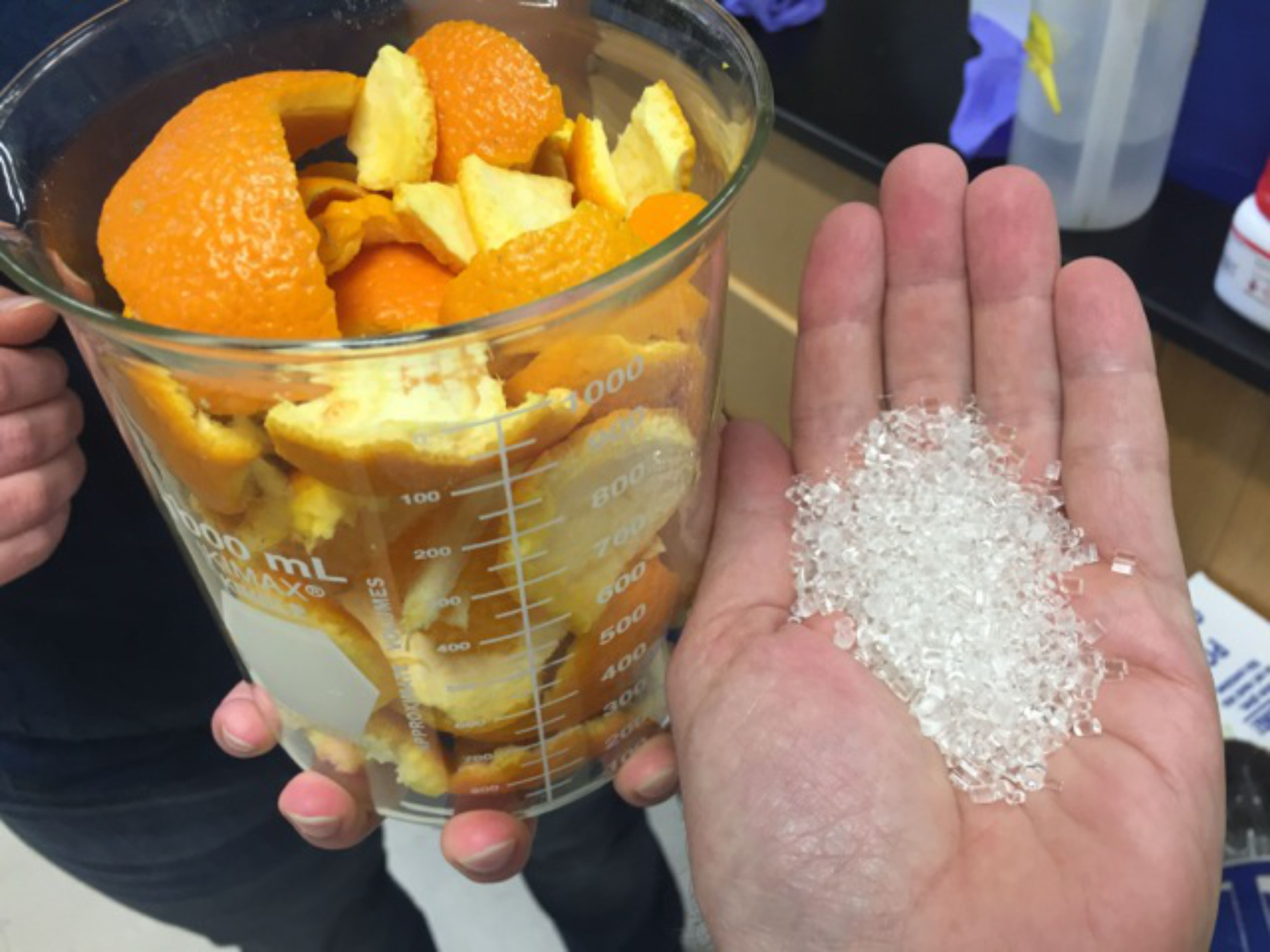 Photo of a person's hand holding polymers created by combining CO2 with limonene from orange peels (the photos also shows a container of orange peels ).