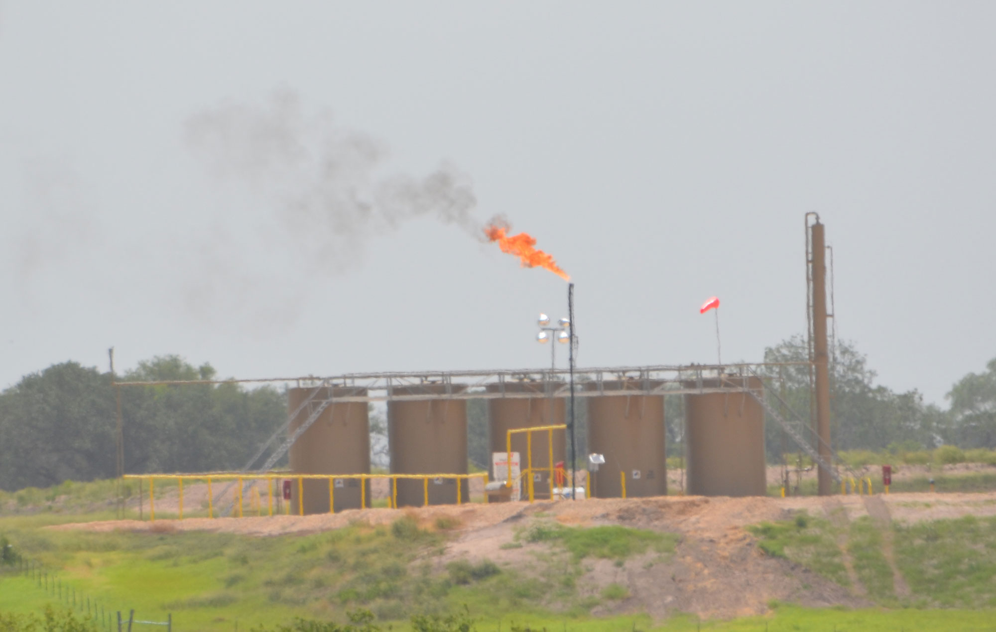 Photograph of gas flaring in the Eagle Ford Shale. The flare appears to be a tall pipe with a flame coming out of the top. Thin black smoke is produced by the flame.