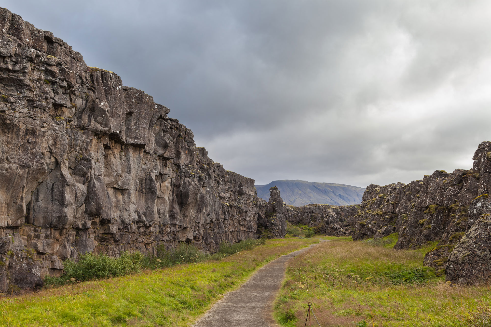 Photo of Almannagja fissure in Iceland showing a trail in a valley with steep cliffs on the right and shorter cliffs on the left. This rift is part of the Mid-Atlantic Ridge.