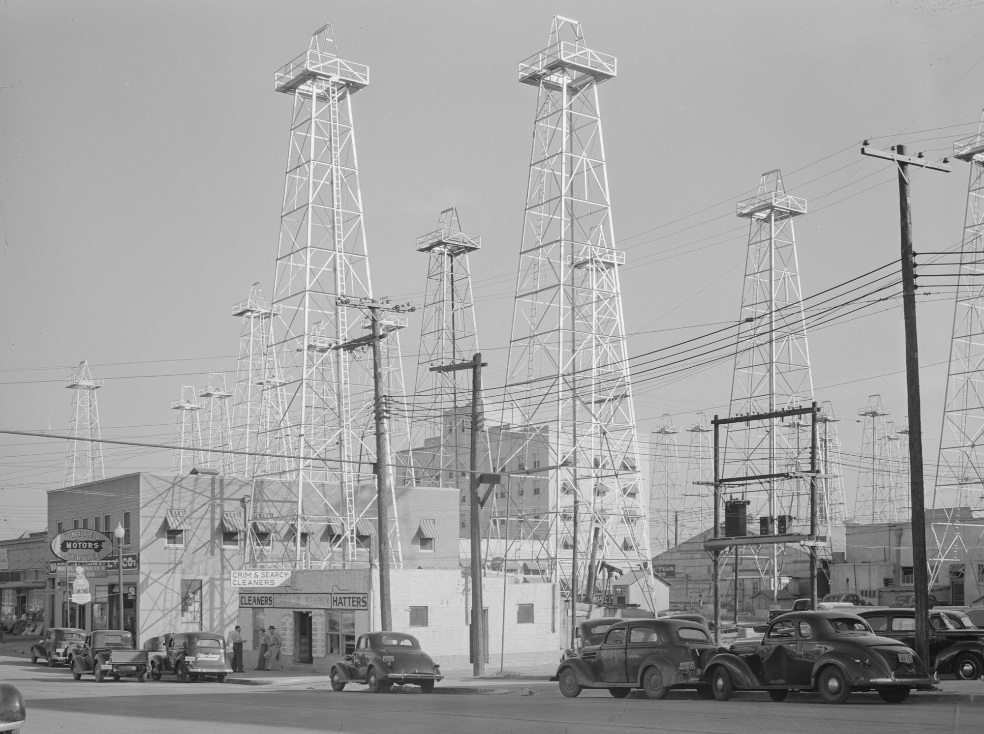 Black-and-white photograph of oil derricks in Kilgore, Texas, East Texas Oil Field, 1939. The derricks are placed among buildings of the town.