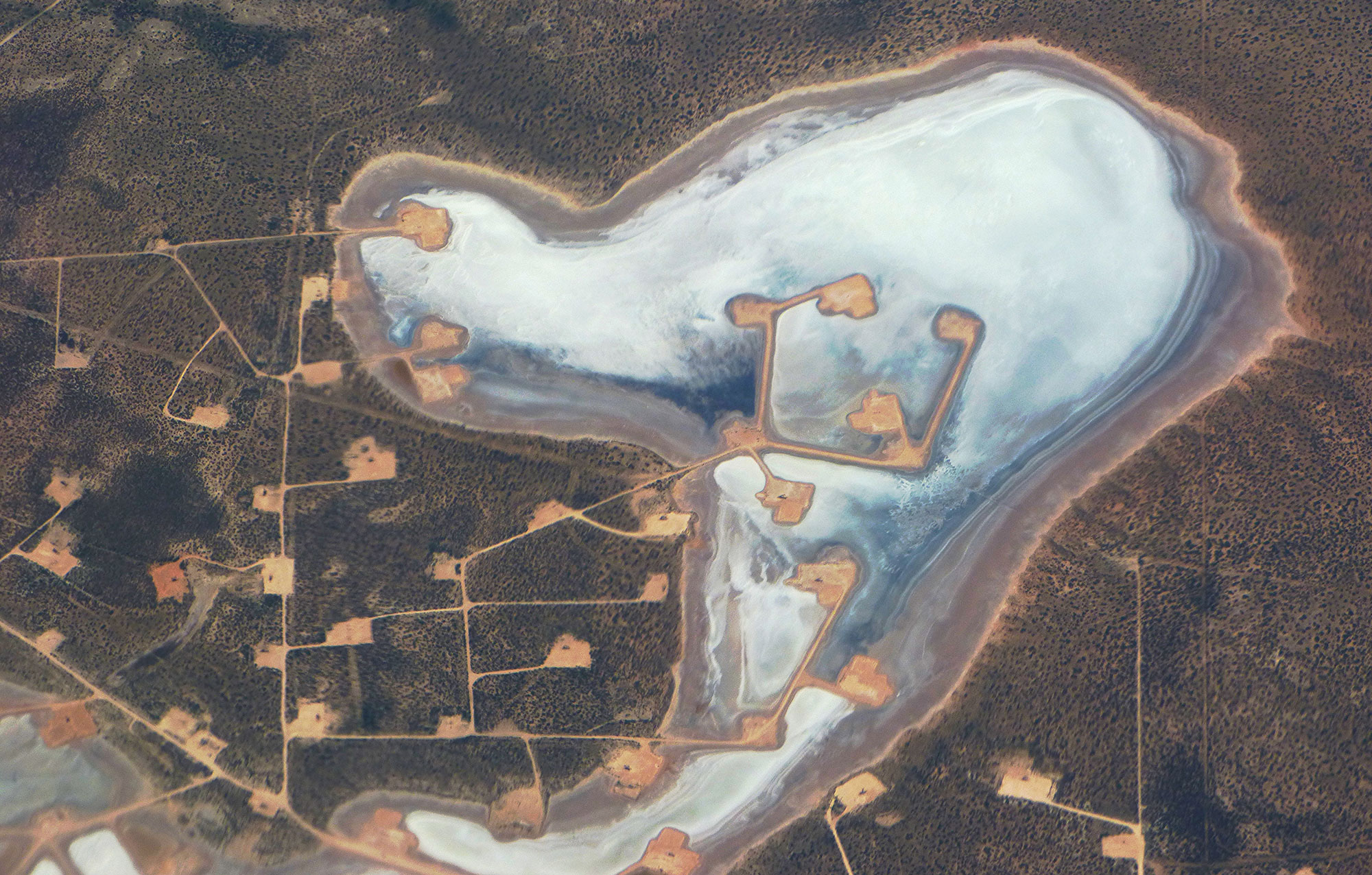 Aerial photograph of Juan Cordona Lake and surrounding land in west Texas showing development for oil and gas extraction. The photo shows a network of roads and oil well pads on the landscape and extending into the lake.