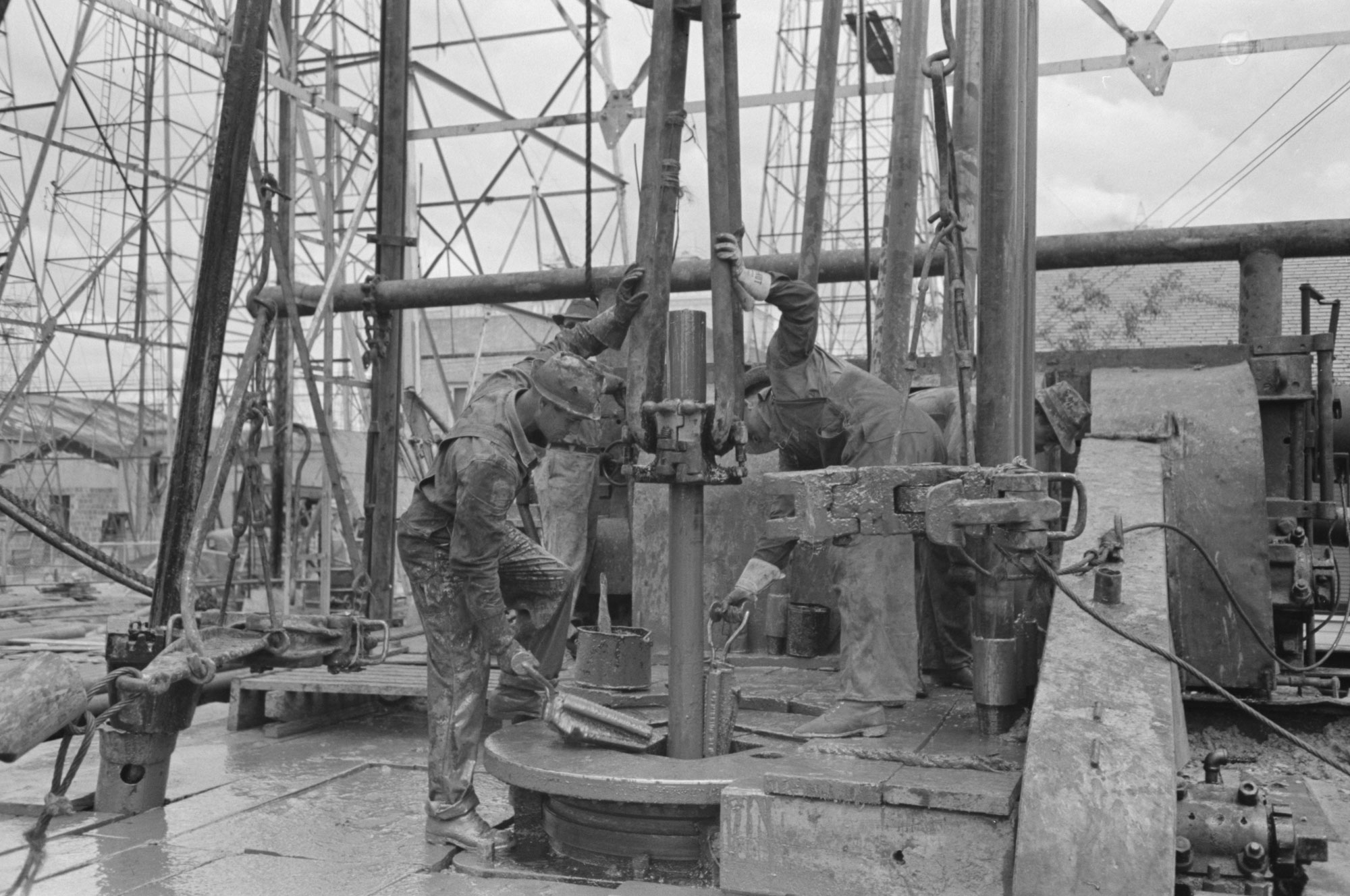 Black and white photo of three men working on an oil well in Texas in 1939. The men are pulling a piece of pipe out of the well.