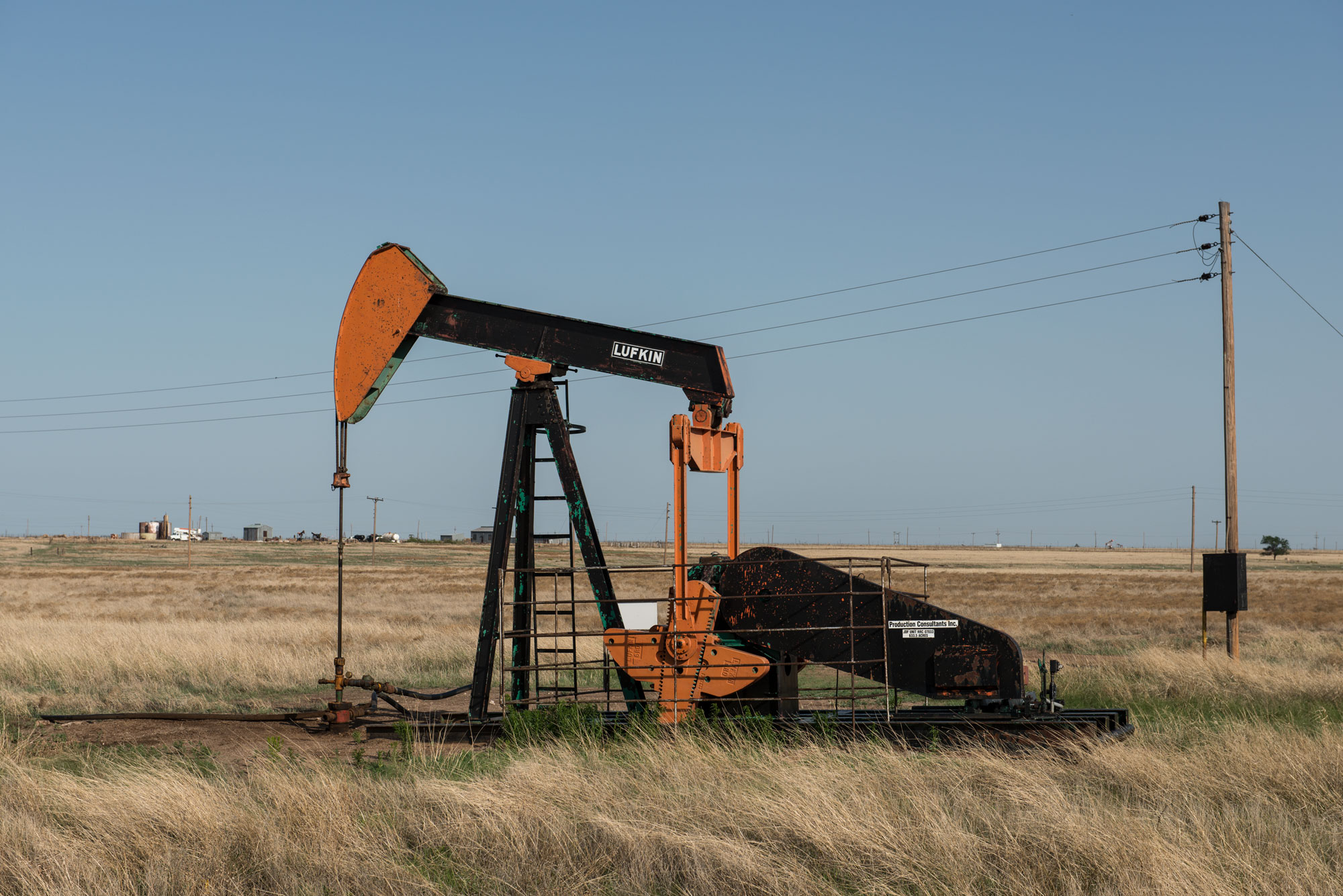 A photograph of a black and orange pumpjack in a field of dry grass.