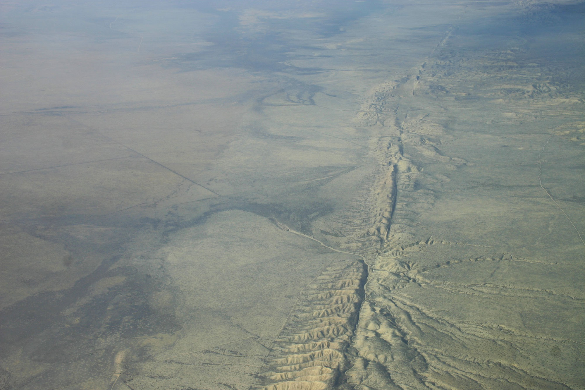 Aerial photo of the San Andreas fault running through a flat plain. The fault looks like a ridge with a trench running through its center.