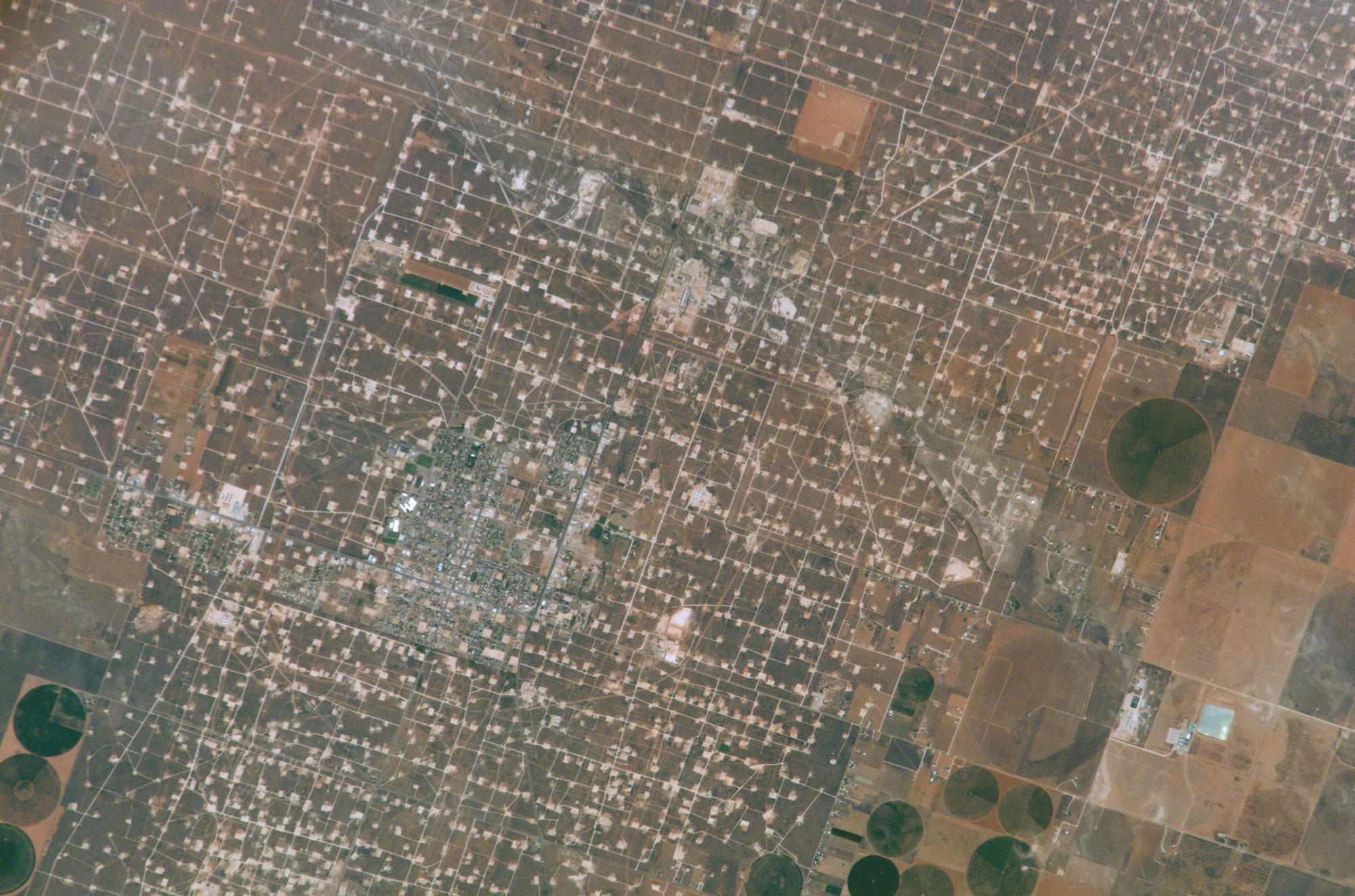 Photograph taken from space by an astronaut showing development for oil extraction in Wasson Oil Field, Texas. The photo shows a rough grid of roads and pads for oil wells.