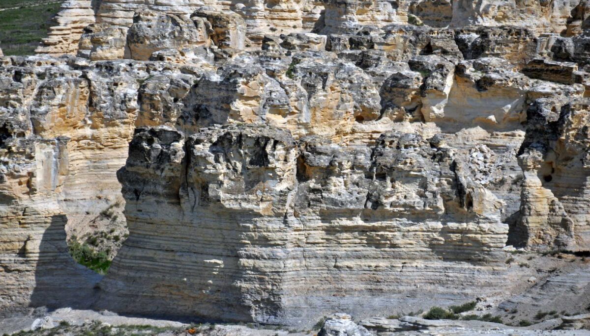 Photo showing Niobrara Chalk bluffs in western Kansas. The bluff are made of soft gray-and-beige rock. Near the ground, the chalk shows horizontal bedding. The tops of the bluffs are more weathered and irregular in appearance.