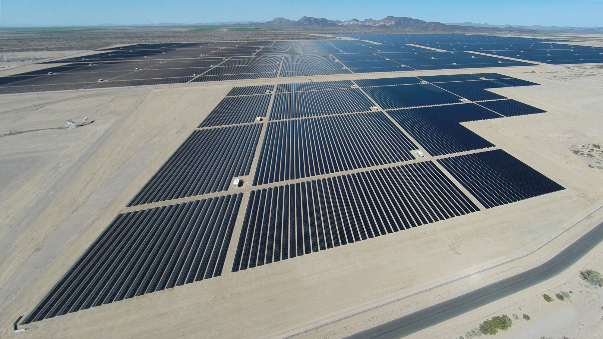 Photo of the Agua Caliente solar farm, Arizona. Photo shows arrays of solar panels arranged in multiple grids on a flat, barren landscape. Mountains can be seen on the horizon.