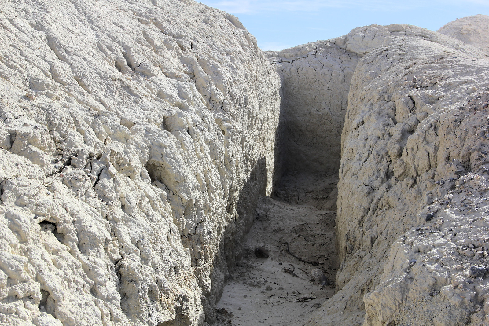 Photograph of a narrow, deep trench with a flat bottom dug into very dry, off-white sediment at Tule Springs.