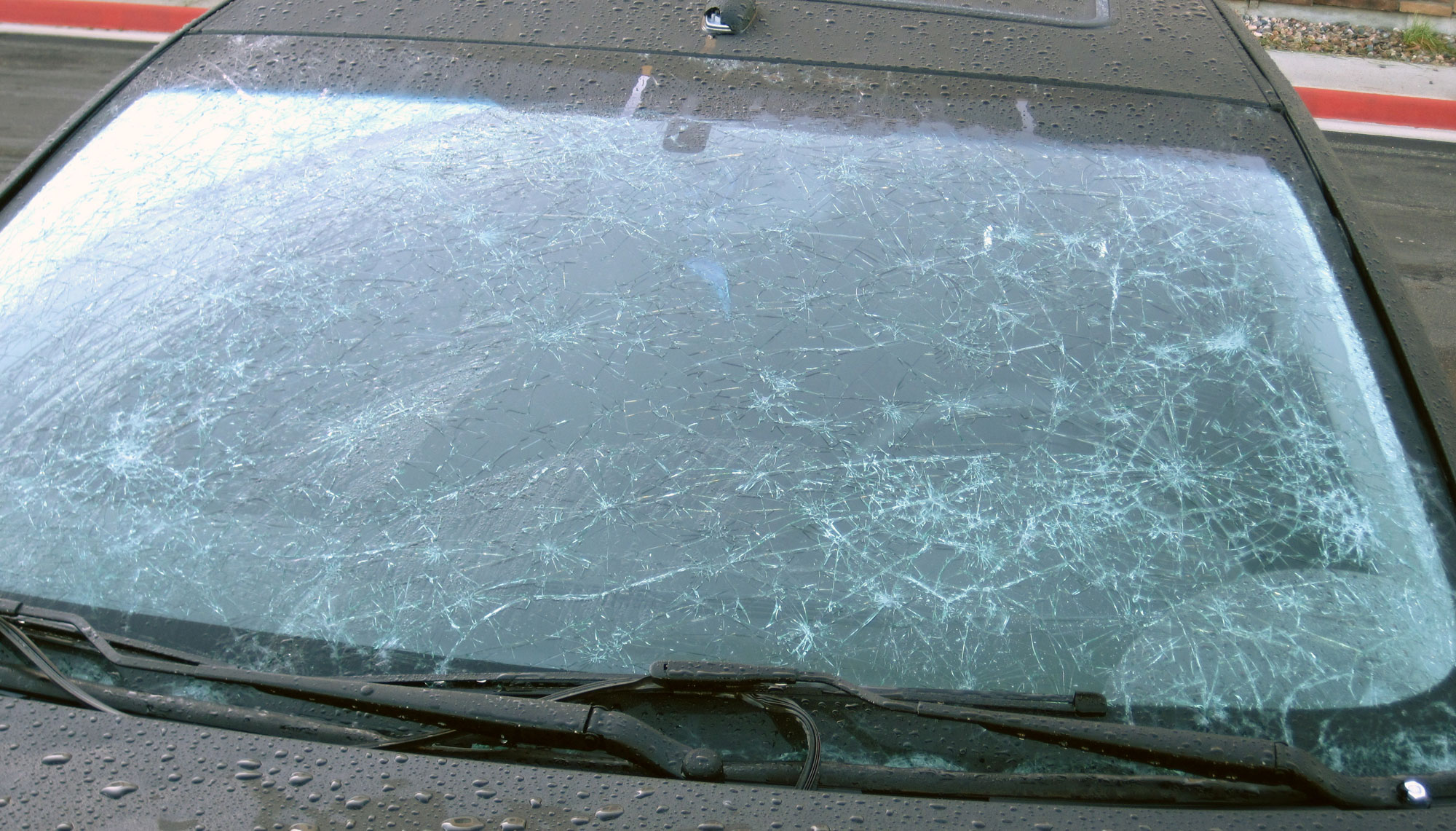 Photograph of a car windshield showing impact marks with radiating cracks where hailstones hit the glass.