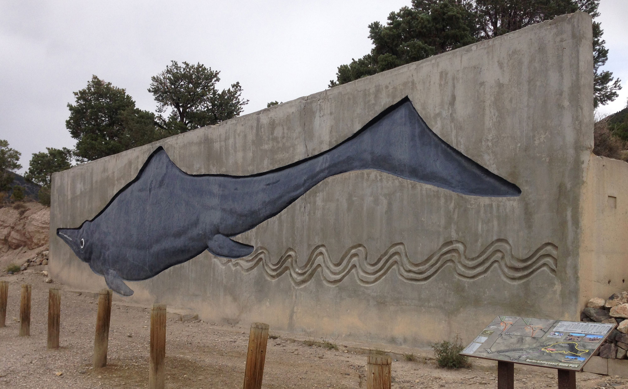 Photography of a cement wall with a large ichthyosaur in relief. The ichthyosaur is painted gray.