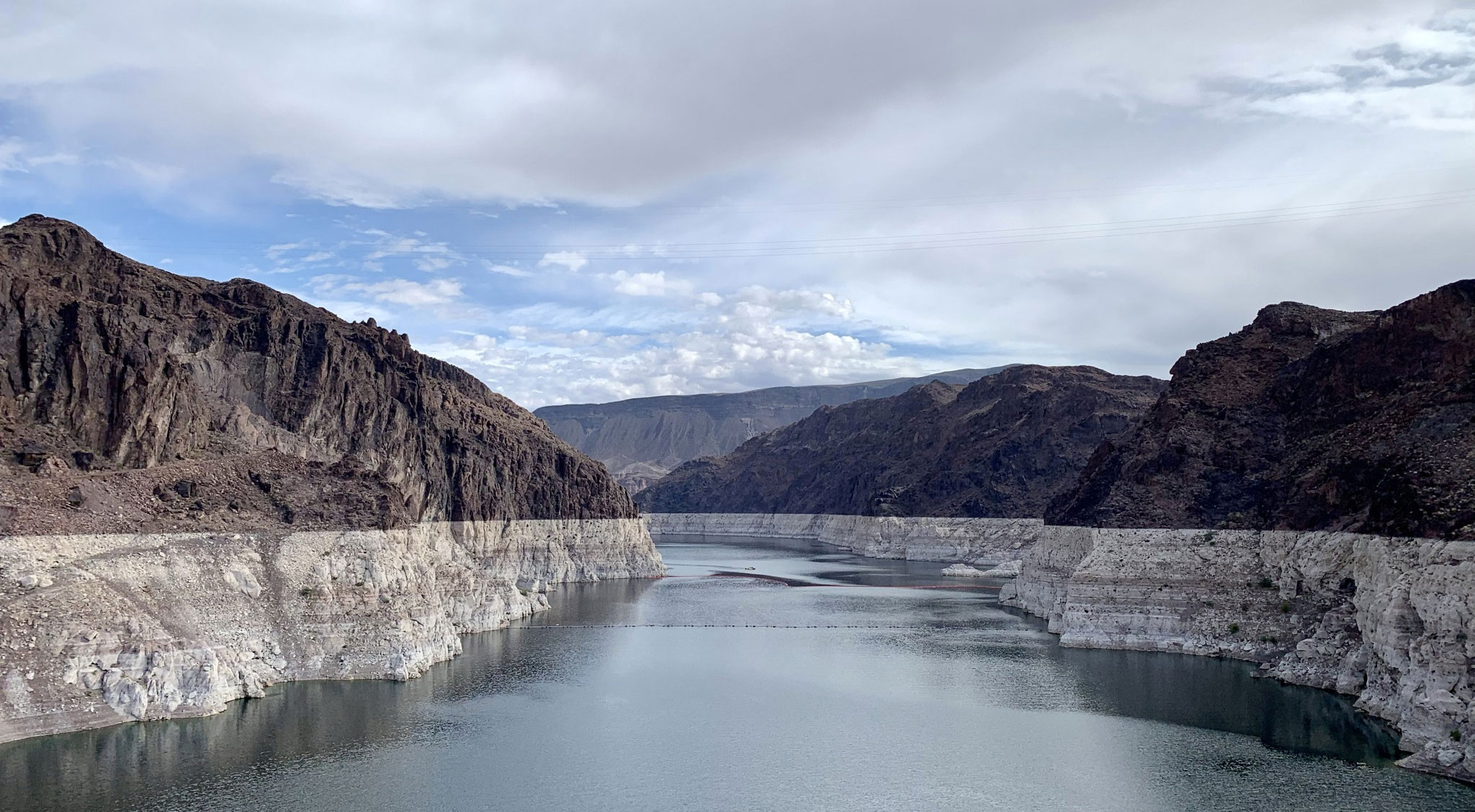 Photograph of Lake Mean behind the Hoover Dam, Arizona-Nevada border. The photo shows a narrow lake between hills on either side. The rocks making up the hills are dark brown above and off-white near the surface of the lake.