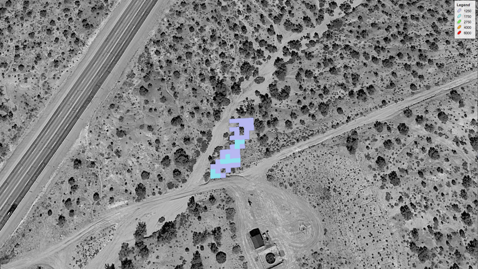 Grayscale satellite image of a dry landscape dotted with sparse trees and cut up by roads and a clearly that may be a wellpad. In the center of the image, blue and purple squares indicate the presence of a methane leak detected using specialized satellite equipment.