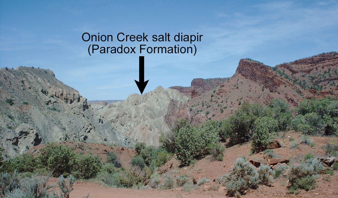 Photograph of the Onion Creek salt diapir in Utah. The diapir looks like an outcropping of light gray rock between an outcrop of red rock to the right and an outcrop of darker gray rock to the left.