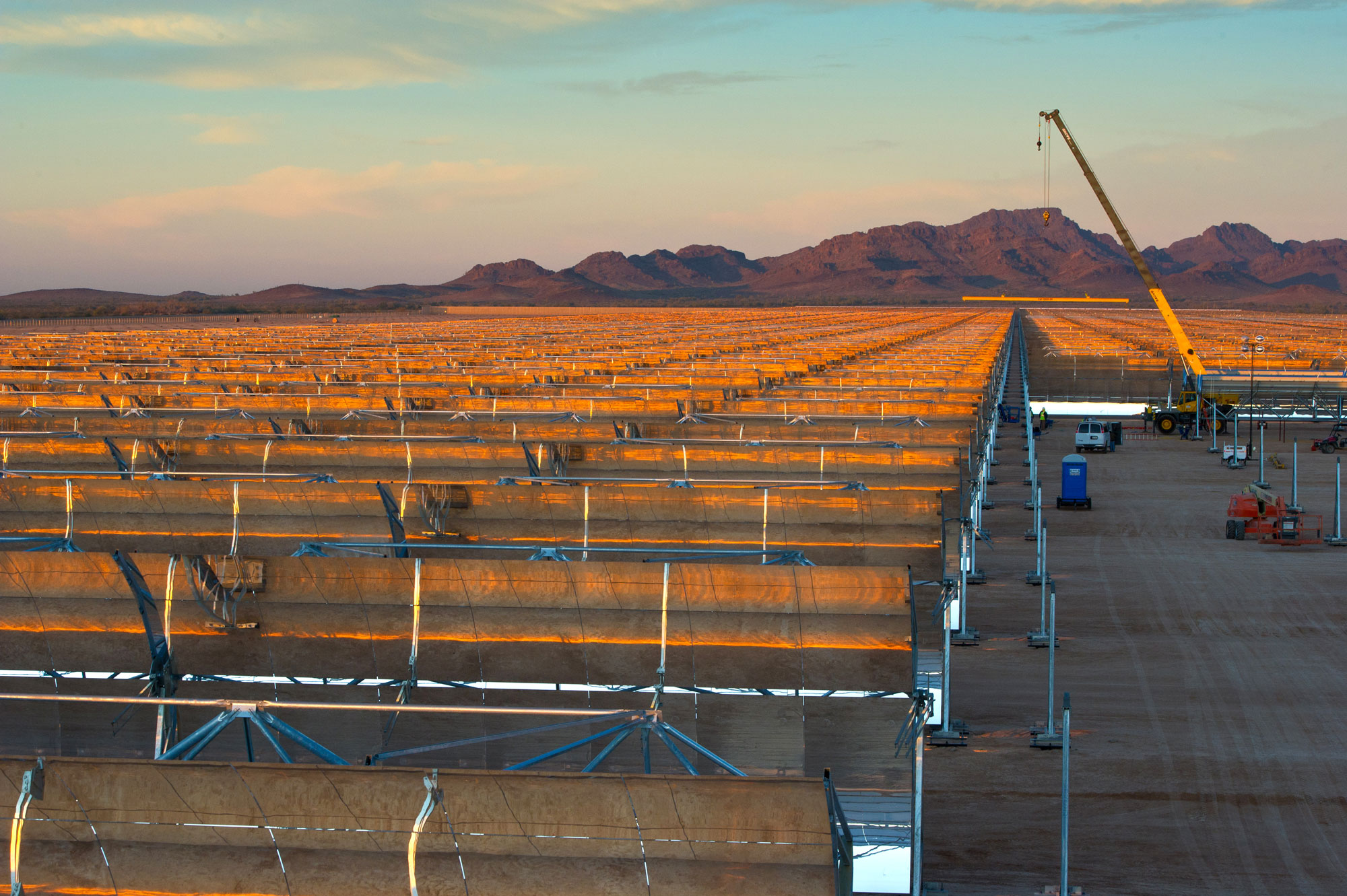 Photograph of a solar plant in Arizona. The plant is under construction, as indicated by a crane in the background. The plant is made up of many rows of parabolic mirrors.