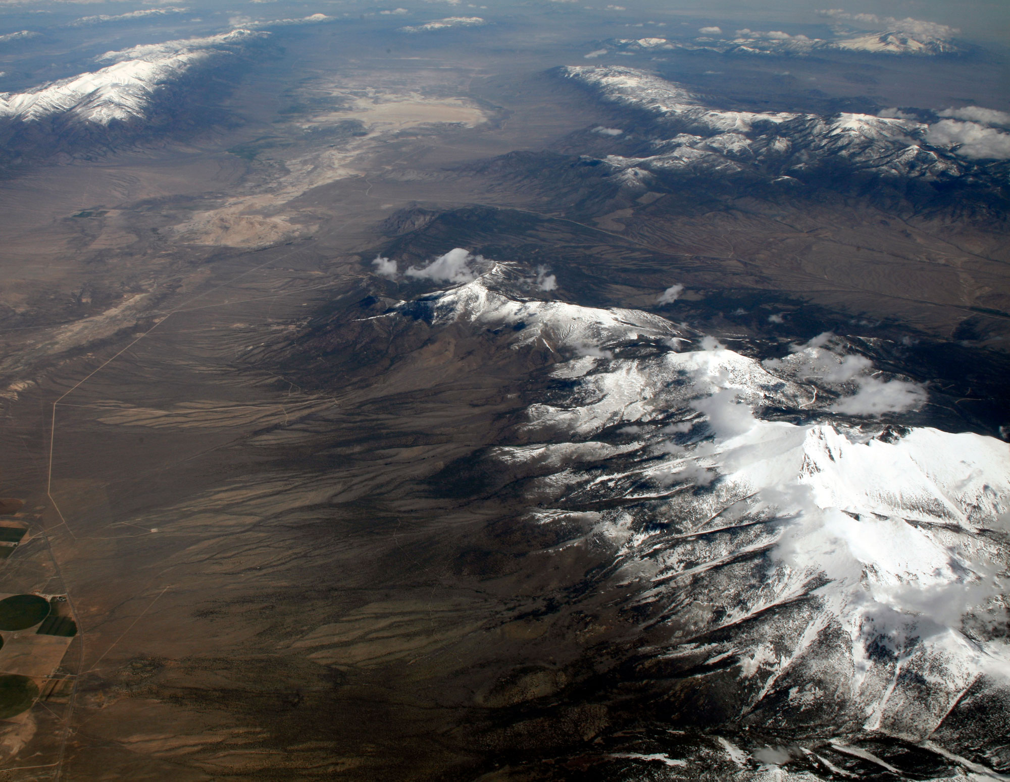 Aerial photograph of Wheeler Peak in Great Basin National Park, Nevada. The photo shows a dry landscape with mountain chains separated by basins. The mountain peaks are covered with snow.