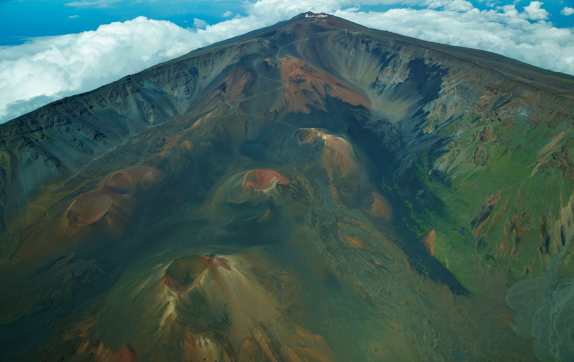 Photograph of cinder cones on Haleakala volcano, Maui. The photo shows the summit of a volcano with cinder cones on its flank. Each cone is conical in shape with a central depression.