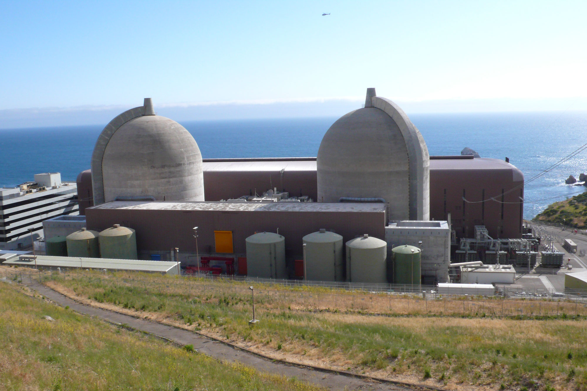 Photograph of the Diablo Canyon Nuclear plant showing two dome-like reactors and other structures. The ocean can be seen in the background.