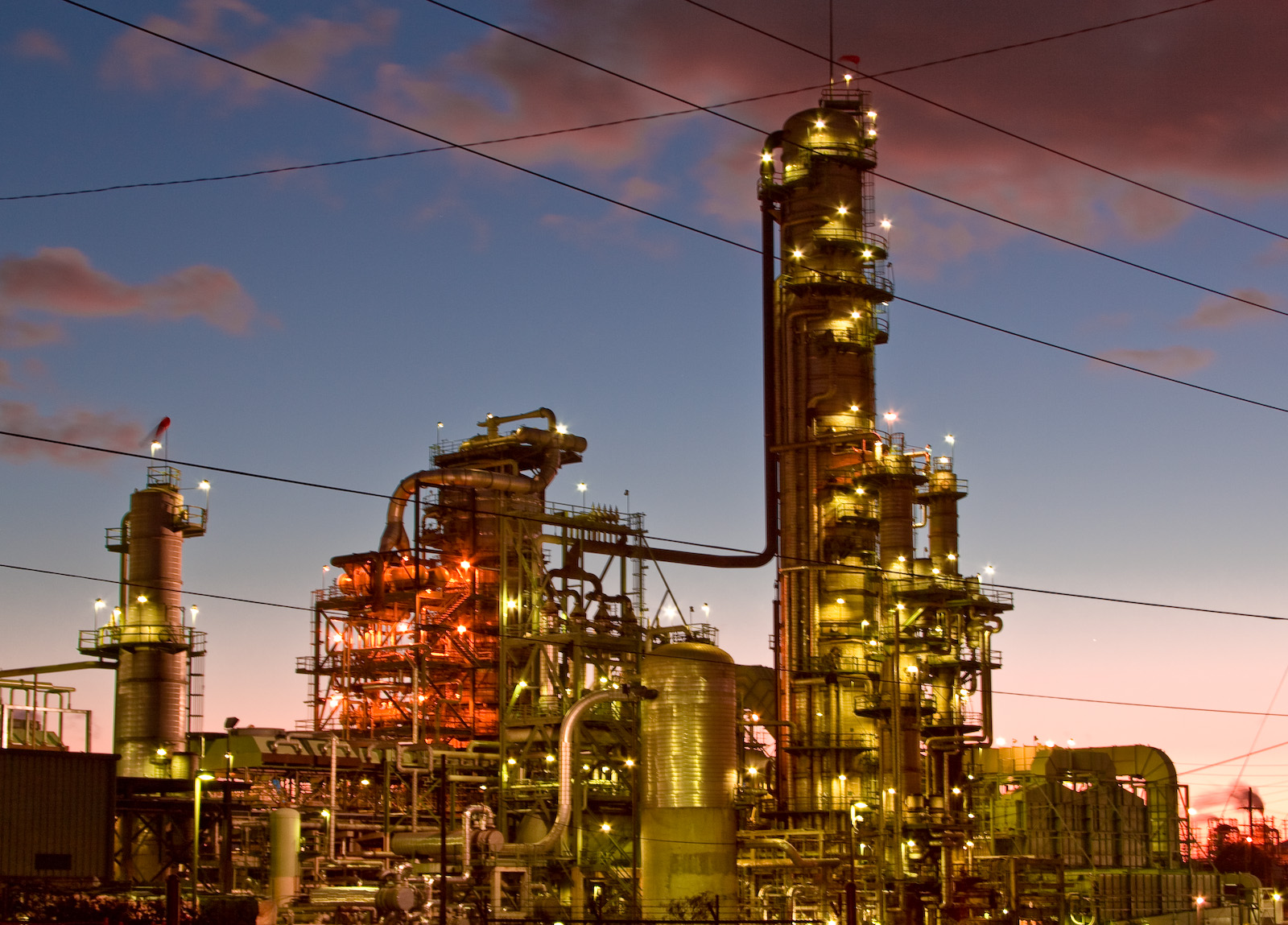 Photograph of the El Segundo Refinery in Westchester, Los Angeles. The photo appears to have been taken at down or dusk. The refinery is lit with many lights. 