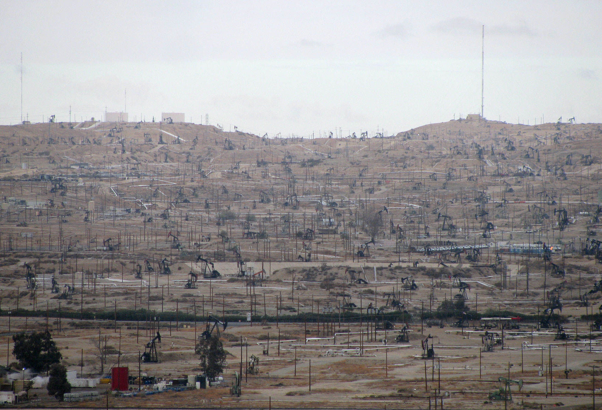 Photograph of the Kern River Oil Field in California taken at ground level. The photo shows a dry landscape heavily dotted with pumpjacks, power poles, and other structures related to petroleum extraction. 