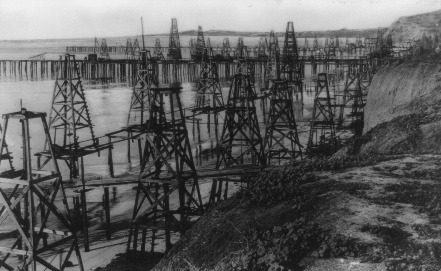 Black and white photograph showing numerous oil derricks on the coast and in the water in Summerfield, Long Beach, California, ca. 1920.