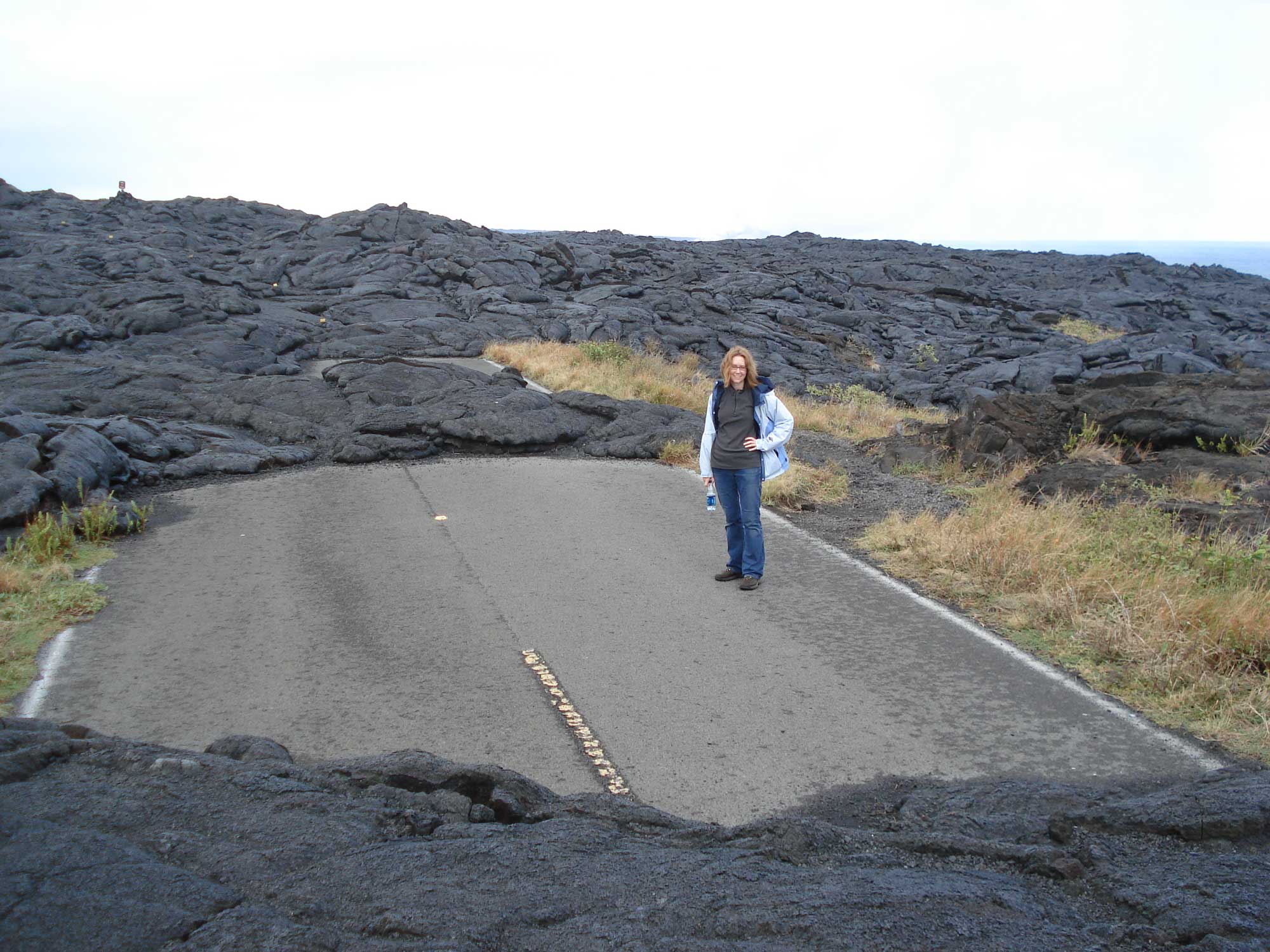 Photograph of a woman standing on a road on Hawaii Island that has been partially covered by lava.