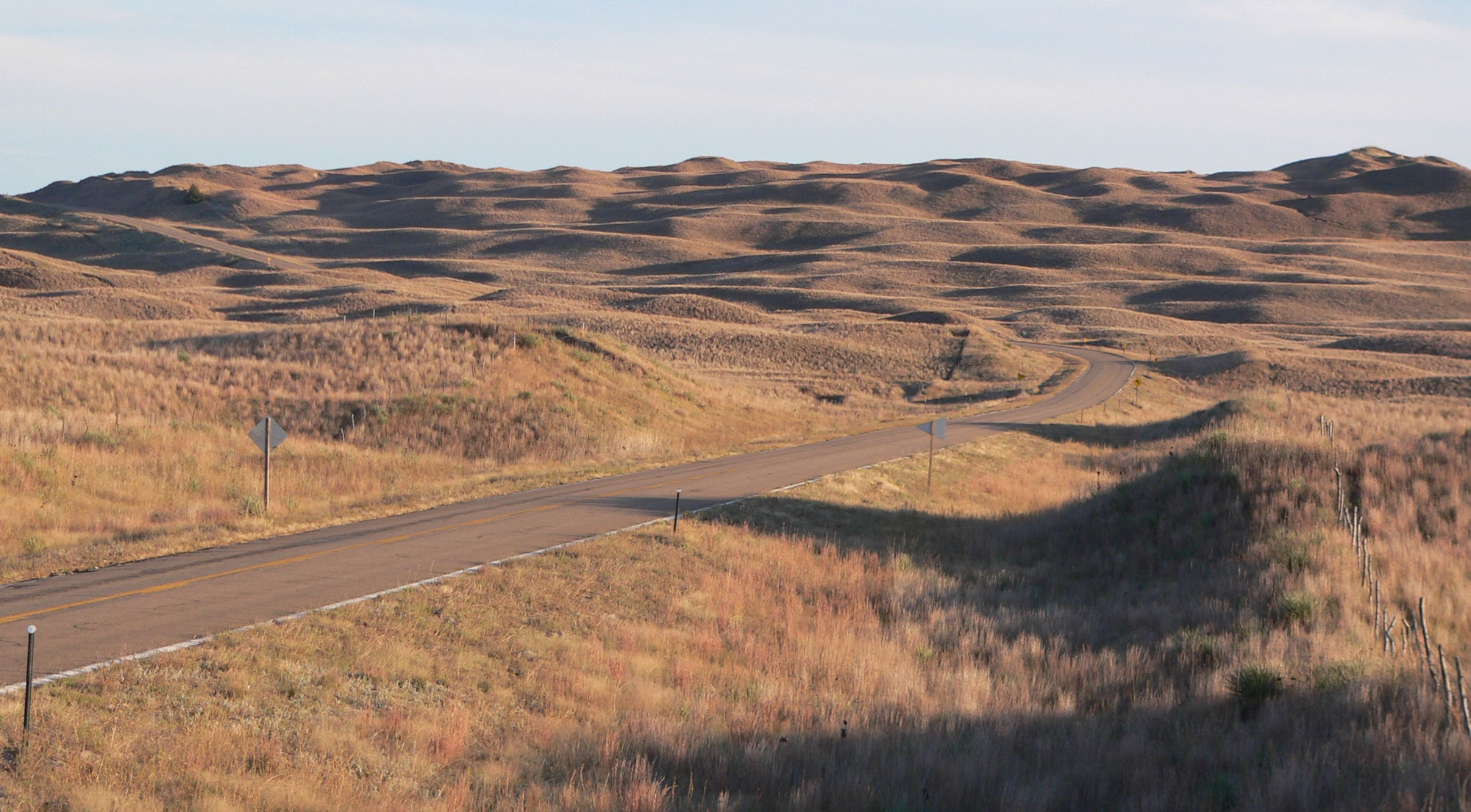 Photo of the Nebraska Sandhills. The photo shows low, rolling hills covered by dry yellow to brown grass.