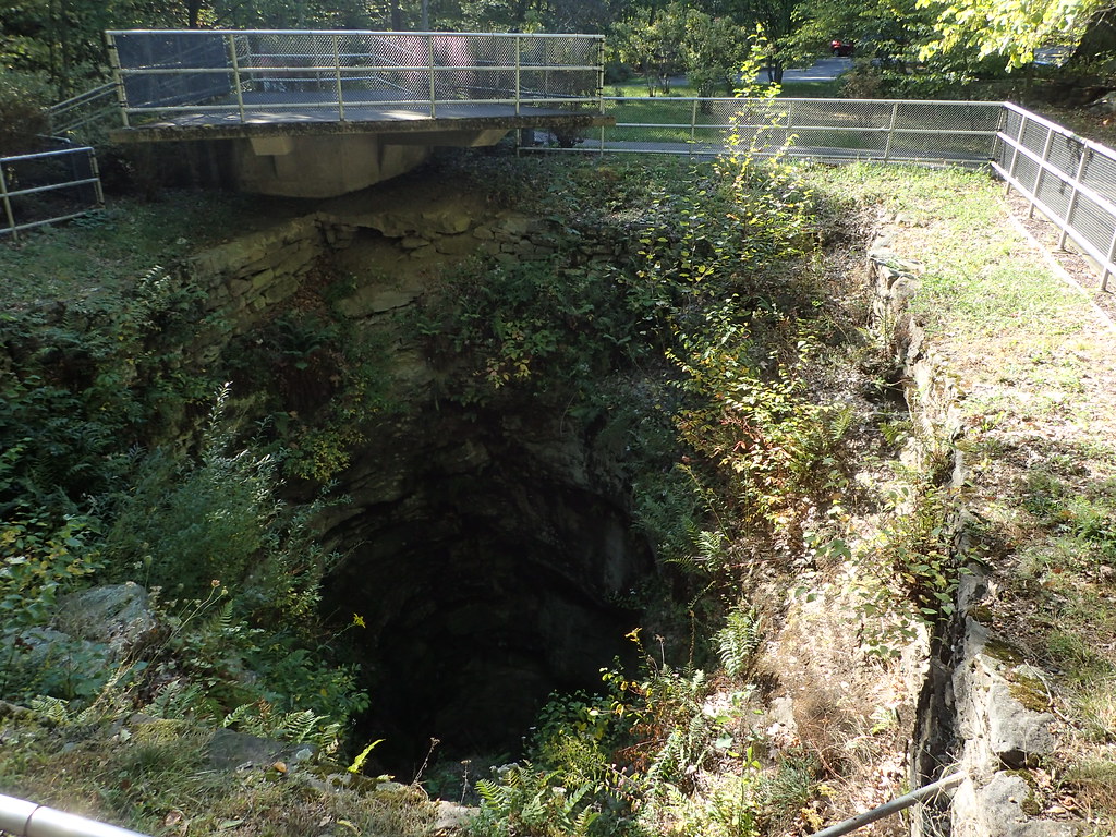 Photograph of the large pothole at Archbald Pothole State Park. The photo shows a large, round, deep hole surrounded by a fence. The bottom of the hole cannot be seen.