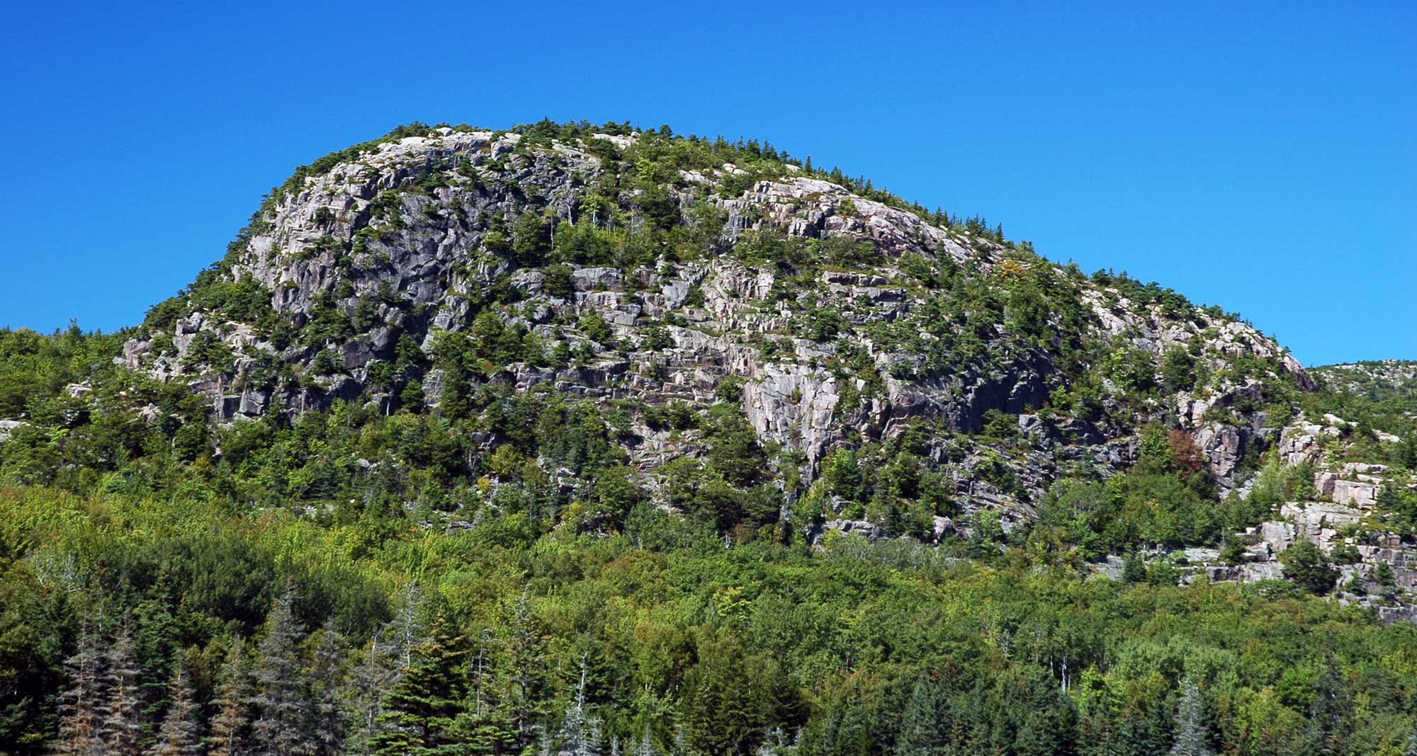 Photograph of "The Beehive," a rock formation at Acadia National Park, Main. The photo shows a rounded rock outcrop with a steep slope on the left and a gentler slope on the right. This outcrop was shaped by glacial action.