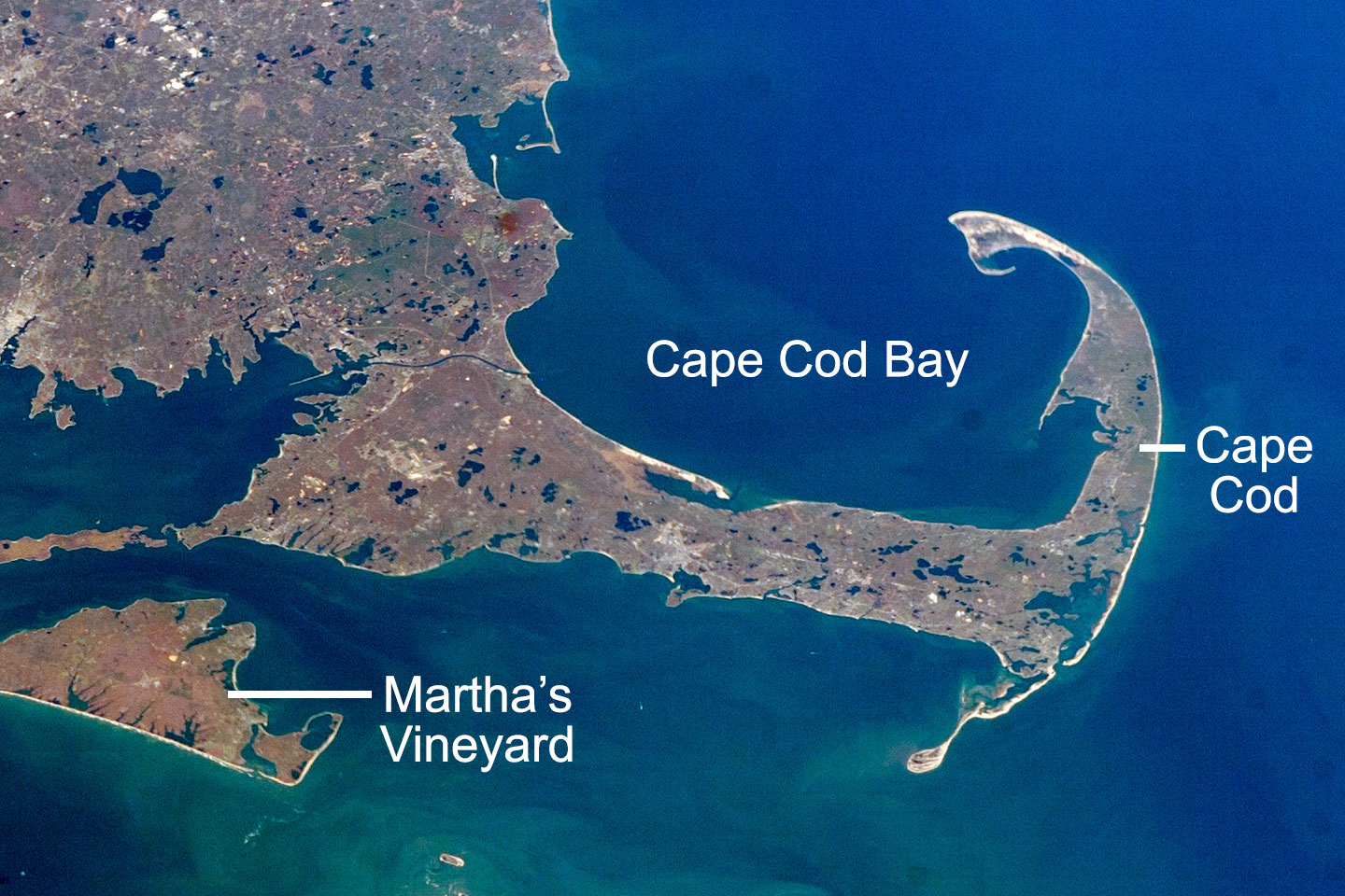 Satellite photograph of Cape Cod, Mallachusetts and Marth's Vineyard. Cape Cope extends like a backwards letter "J" from the southeastern tip of mainland Massachusetts. Martha's Vineyard is an island to its southwest; it is only partially visible in the photo. Cape Cod and mainland eastern Massachusetts have numerous kettle lakes, which can be seen in the image. Cape Cod, Cape Cod Bay, and Martha's Vineyard are labeled.