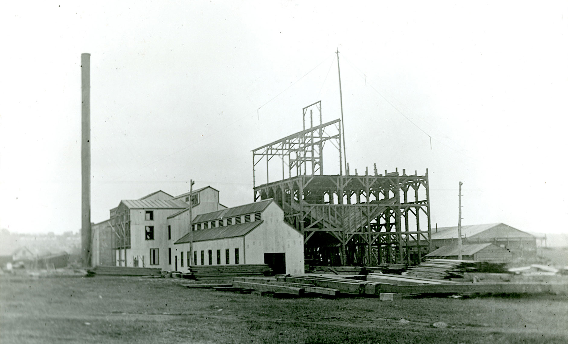 Black and white photo of buildings under construction at the Cranston Coal Mine, Rhode Island, date uncertain. The photo shows a partially completed complex of buildings, some with siding on them and some still being framed. On the left of the complex, a tall structure may be a smokestack. A pile of building material is in the right foreground in front of the structures.