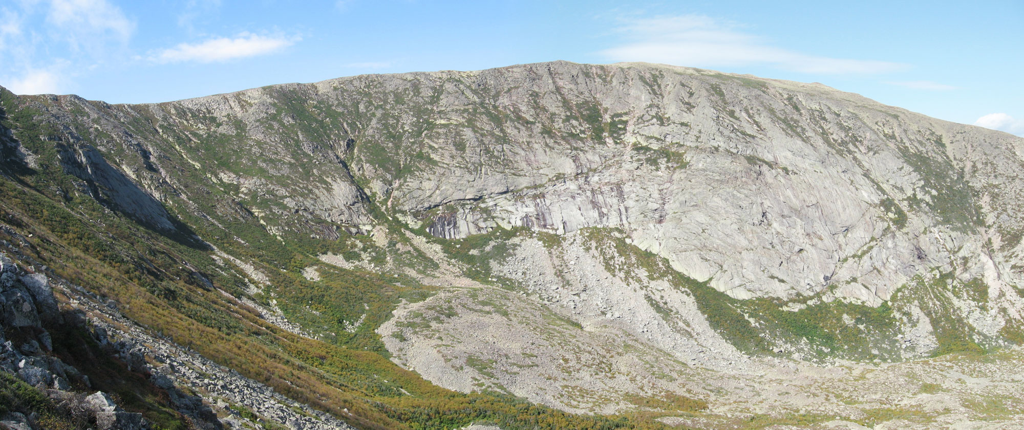 Photograph of the North Basin on Mount Katahdin, Maine. The photo shows a ridge that runs roughly horizontally across the image. The ridge slopes downward to the lower right foreground, where the floor of a basin is visible. The slopes of the ridge are partially vegetated, with unvegetated areas of light gray rock. 