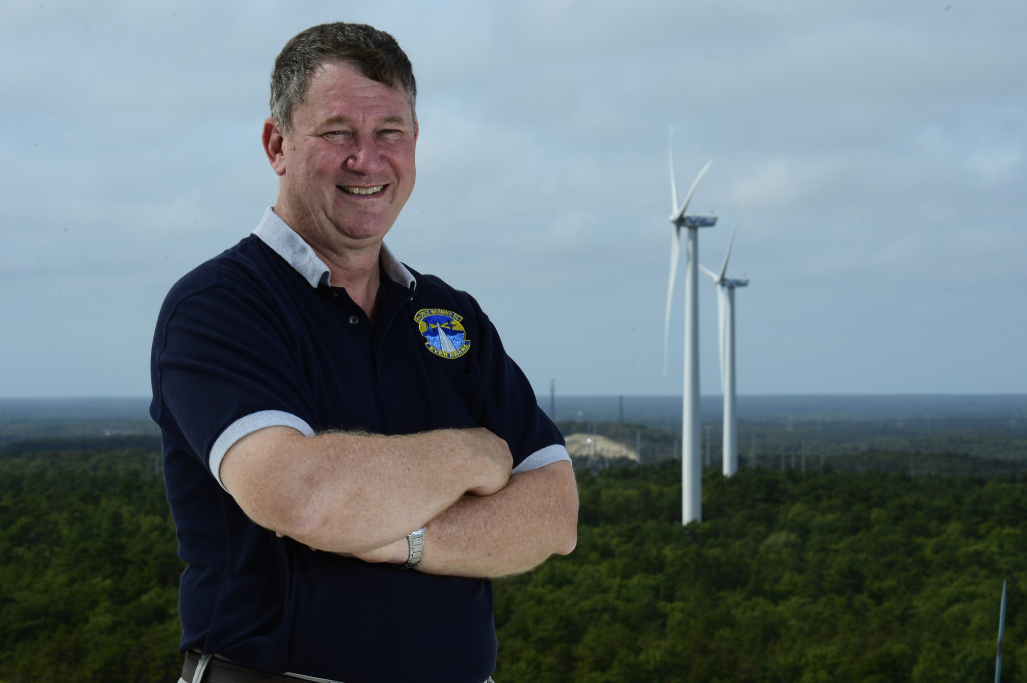 Photo of a man standing in front of two wind turbines in the distance.