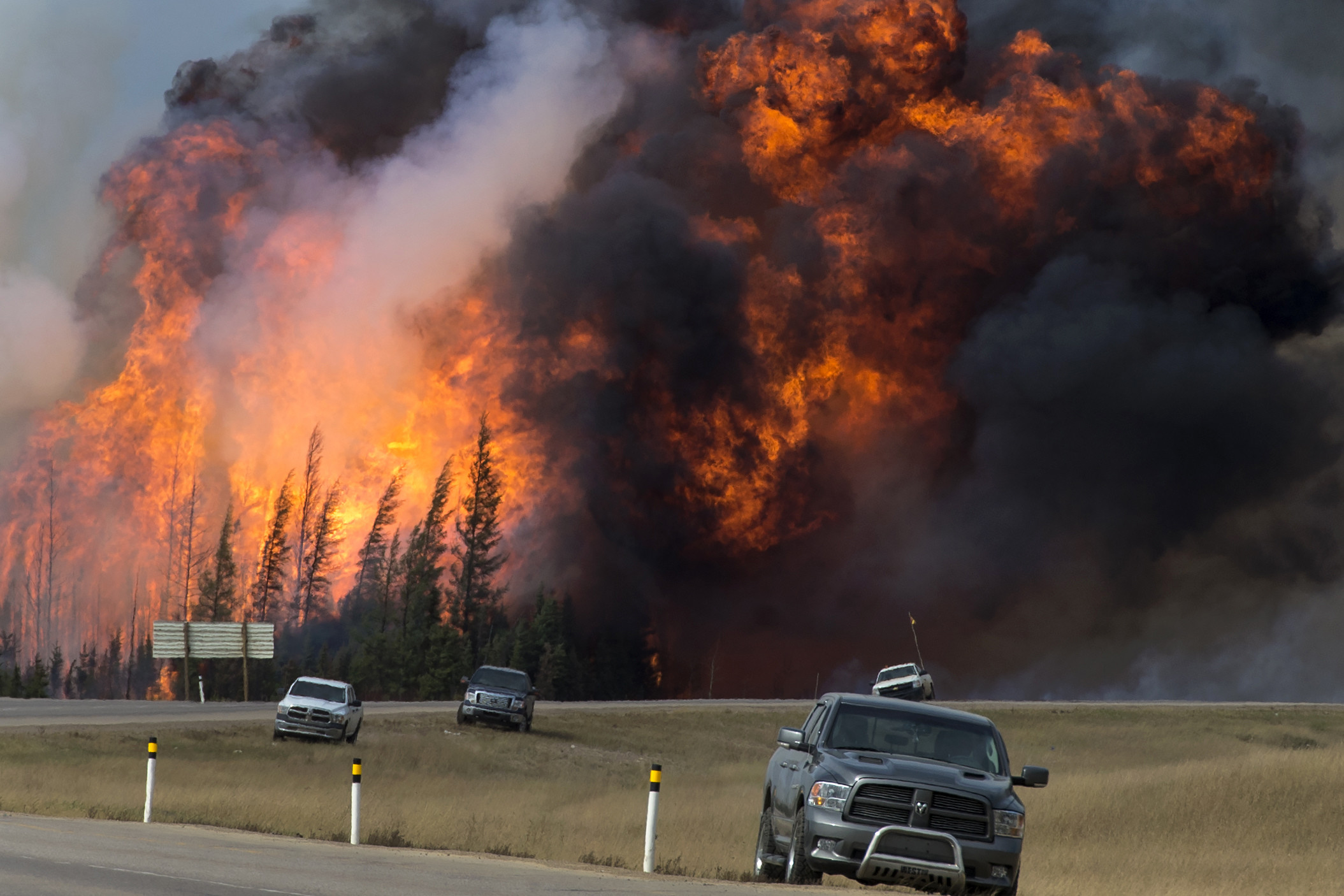Photo of a large forest fire and cars along a road nearby