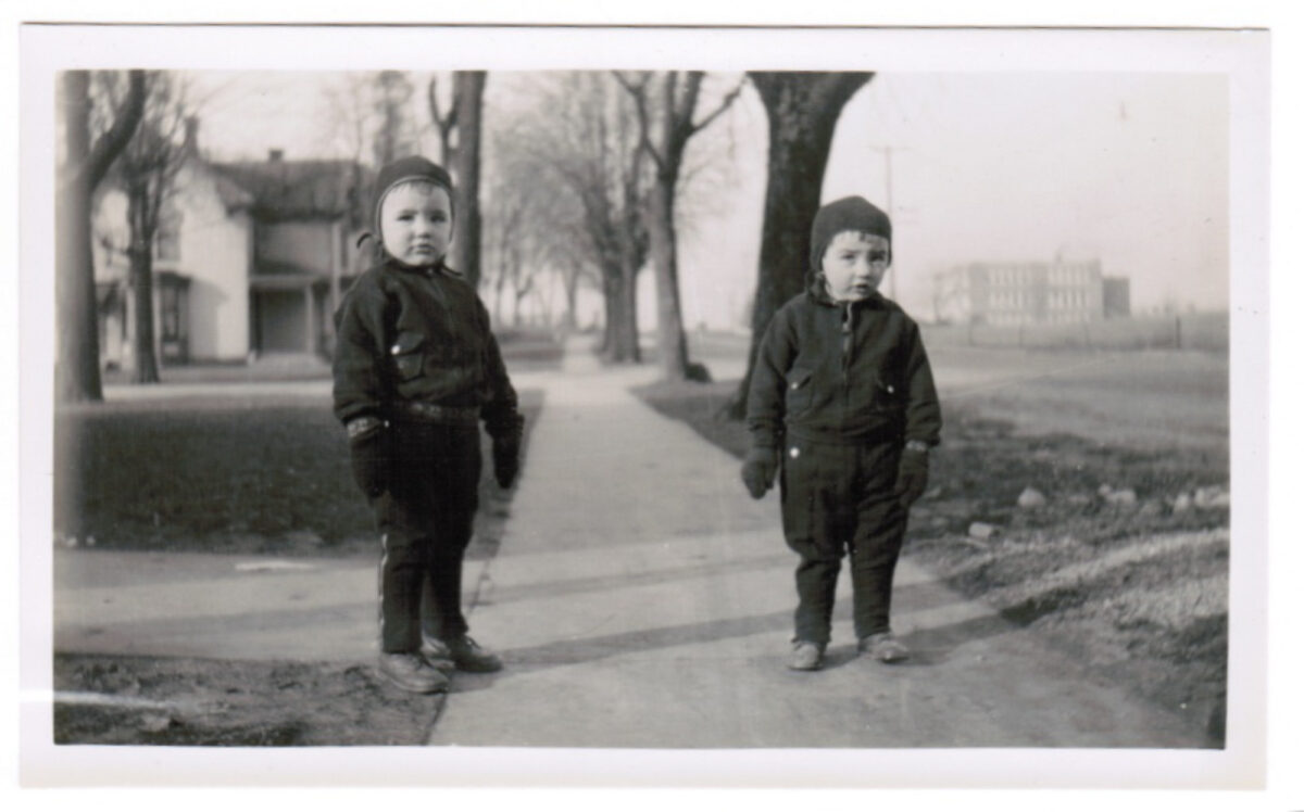 Photo from the early 1900s of two toddlers standing on a sidewalk.