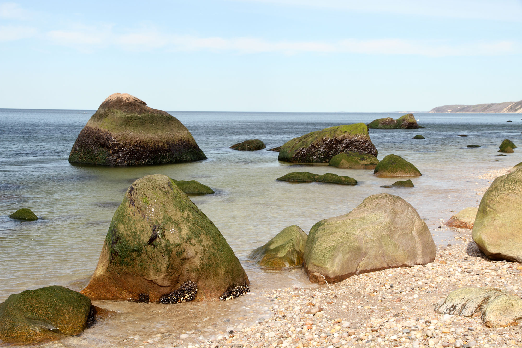 Photograph of glacial erratics on the shore of Long Island in New York. The photo shows large boulders scattered on a beach and in shallow water.