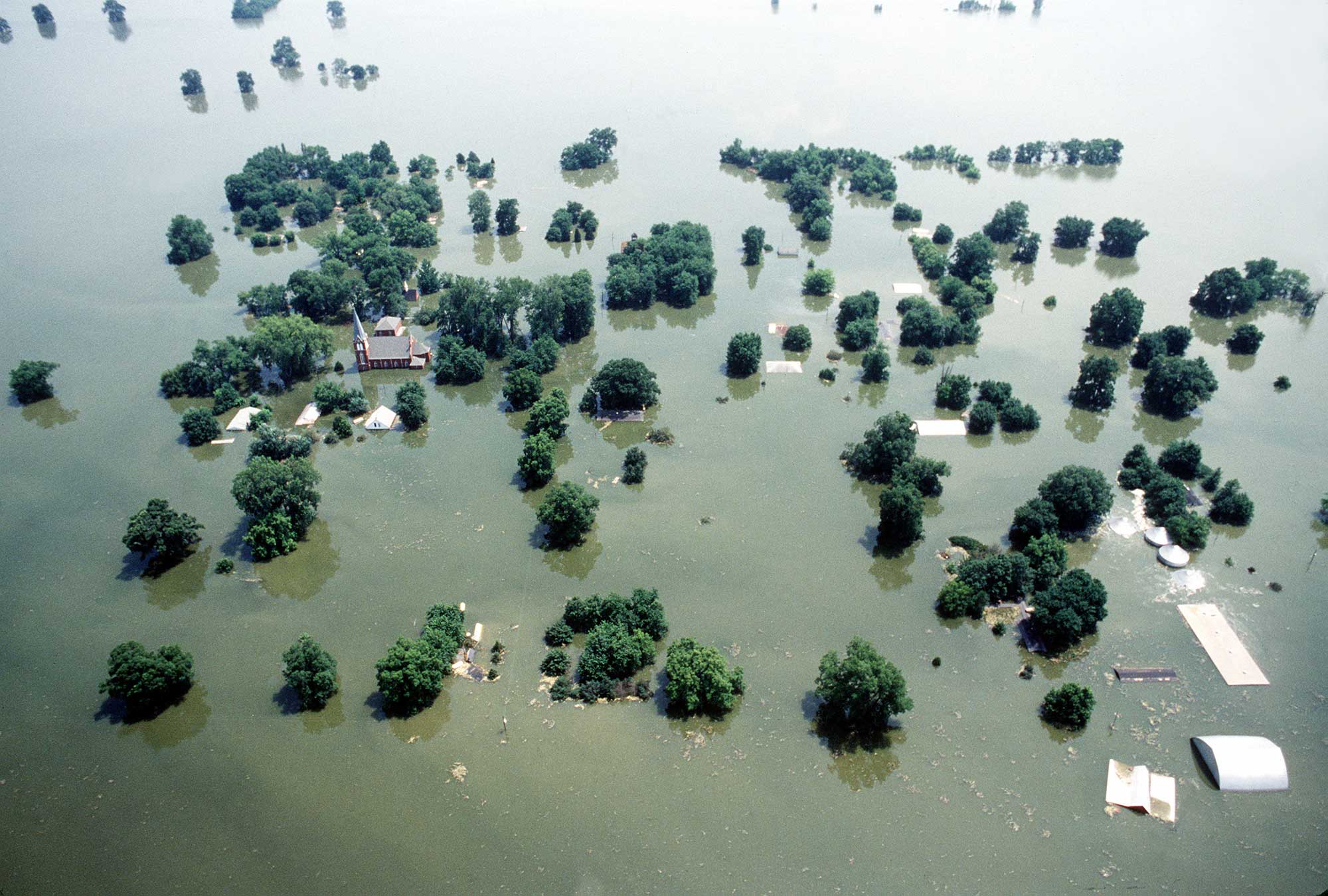 Photograph of flooding in Kaskaskia, Illinois, in 1993. The photo shows a town that is completely flooded, with rooftops and treetops sticking out above the water.