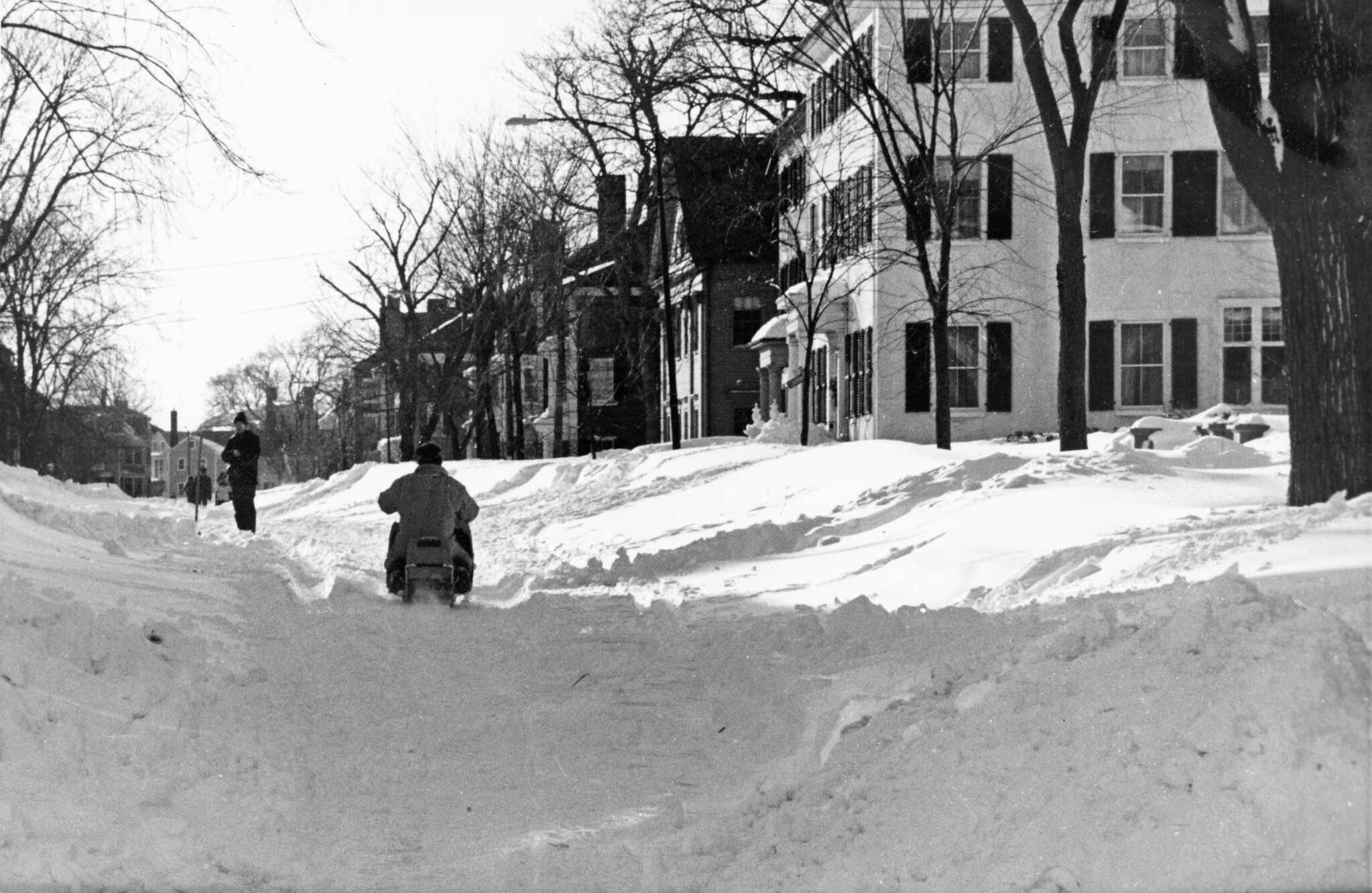 Black and white photograph of a person driving a snowmobile down a snow-covered street in Salem, Massachusetts, following a blizzard in 1993.