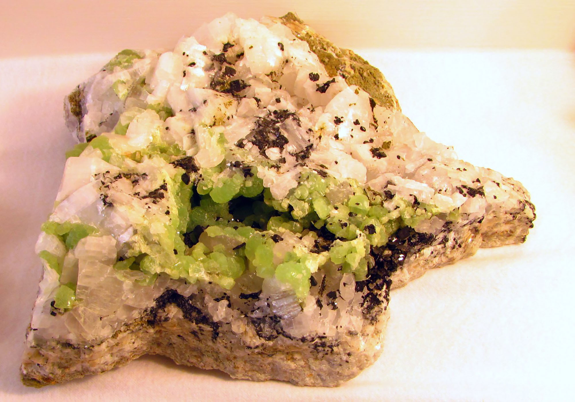 Photo of black babingtonite, green prehnite, and white calcite crystals in a rock from Massachusetts.