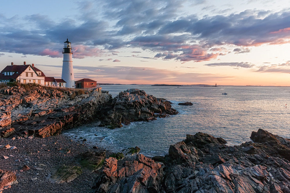 Photo showing the rocky shoreline around a lighthouse at sunrise.